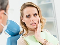Woman in dental chair frowning and holding jaw