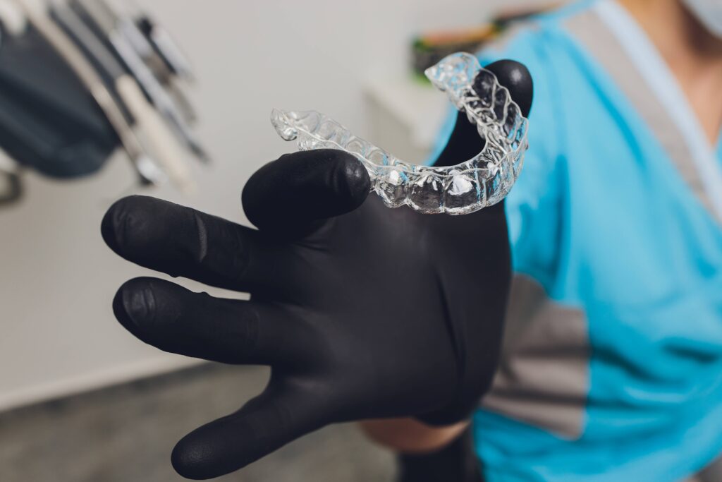 Dentist holding clear aligner with black glove